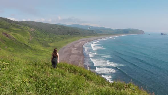 Young Woman Looking at the Ocean Standing on a High Cliff Above the Sandy Beach alt