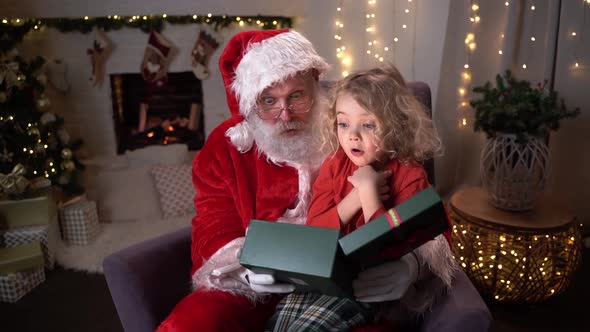 Funny Santa Claus Sitting on His Rocker with Little Cute Boy Sitting on His Knee, Opening Up a Gift