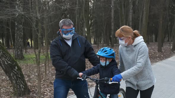 Mom and dad teach their young son to ride a bike in the city Park 