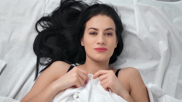 Portrait of Pretty Brunette Young Smiling Woman Lying on Bed alt