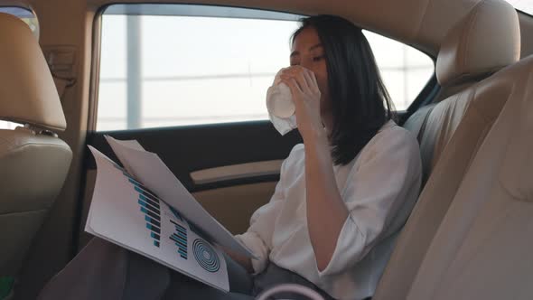 young Asia businesswoman working and drinking disposable paper cup of hot drink in back seat. alt