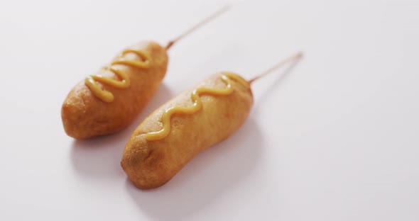 Video of corn dogs with mustard on a white surface alt