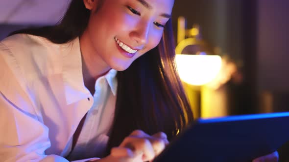 Young Asian beautiful woman enjoy using smartphone- tablet   in bedroom at night time. alt
