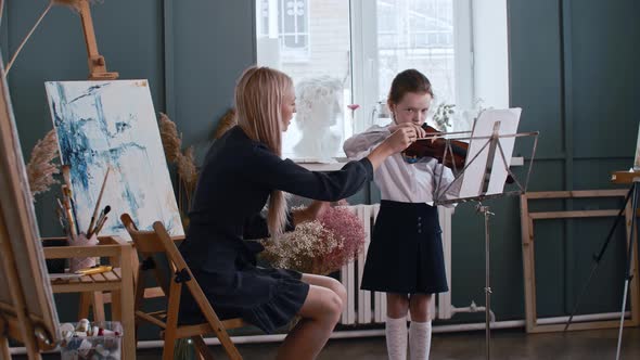 Young Blonde Woman Teacher Teaching a Little Girl How to Properly Hold a Bow While Playing Violin alt