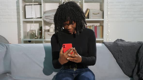 African American Lady with Curly Hair Types on Smartphone alt