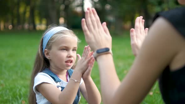 Pretty Little Child Girl Playing Game with Her Mom with Their Hands Outdoors in Green Summer Park alt