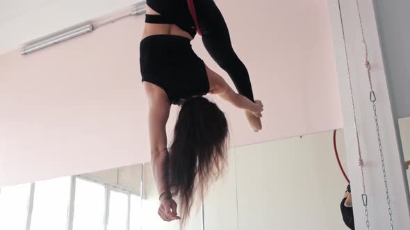 A Young Woman Gymnast Hanging in an Acrobatic Ring Upside Down alt