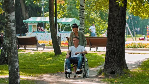 Friends Walking in Park a Man in a Wheelchair and His Female Friend Going in the Deserted Part of alt