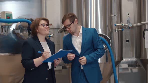 Businesswoman with Clipboard Listening To Manager of Beer Factory alt