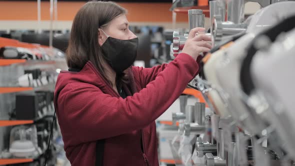 Girl in a Medical Mask Buys a Mincing Machine in a Shop alt