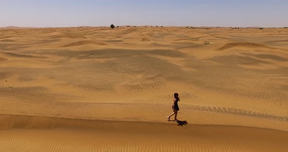 Girl Walks Along a Dune in the Desert.