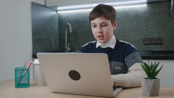 Smiling Boy Chatting Online By Video Call with Laptop Computer at Home While Sitting at the Table alt
