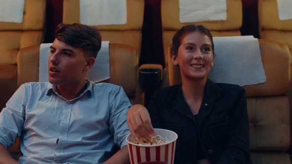 Attractive cheerful young caucasian couple laughing while watching film in movie theater. alt