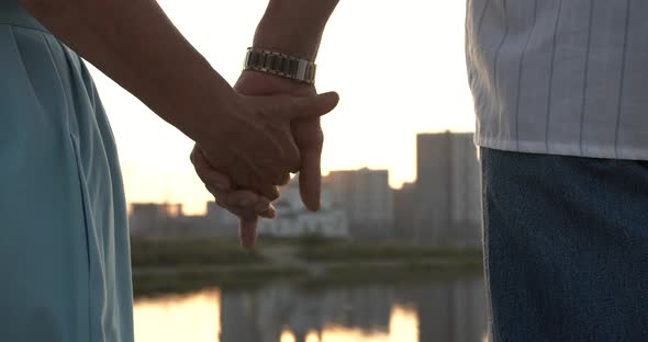 Hands of Elderly People Touch Each Other Against the Background of the City alt