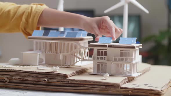 Close Up Of Woman'S Hand Putting The Solar Panel On The Roof Of A Small Model House alt