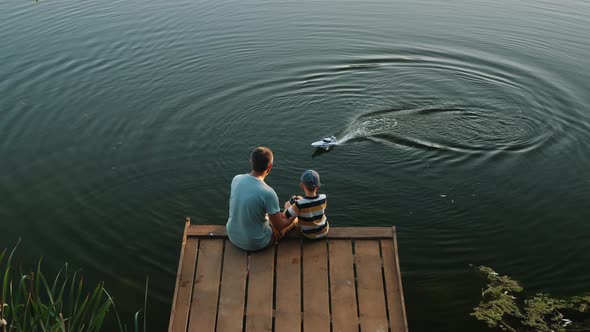 Dad and Little Son Play with RC Toy Speedboat on the Lake alt
