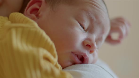 Small Newborn Baby in a Yellow Suit Lies on Mother's Shoulder and Looks Around alt