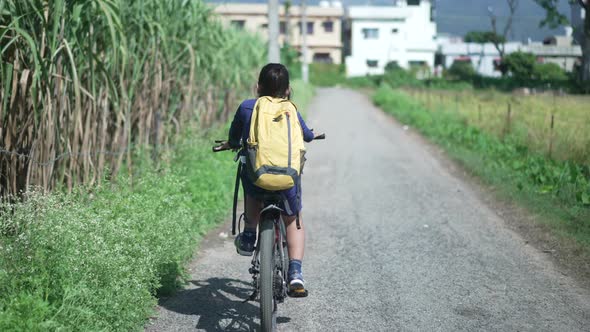 An Indian Kid Cycling on a Road Near a Sugarcane Field in a Rural Area of Uttarakhand India