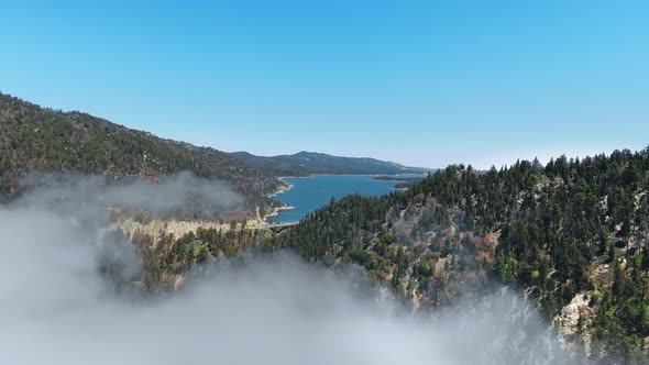 Drone flies over hills in fog towards Big Bear Lake, California, USA alt