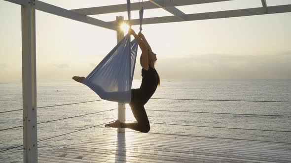Woman Does Yoga Asana Hanging on Aero Yoga Sling on Pier