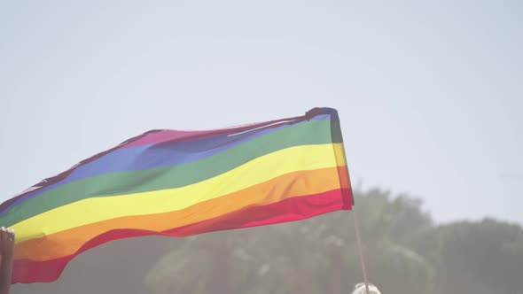 LGBTQ rainbow flag waving in slow motion during a pride parade with thousands of people alt
