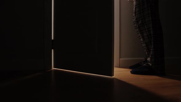 Adult man in a pajamas walks and open the door of the toilet in the night