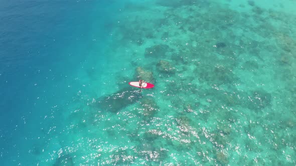 Man Practising SUP Sits on Surfboard with Paddle Among Water alt