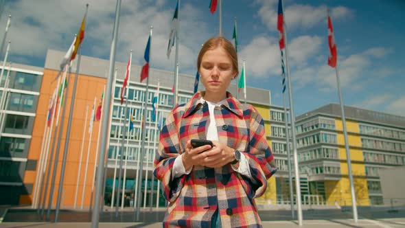 Woman Walks Using Phone App in European Parliament with Flags of EU Countries