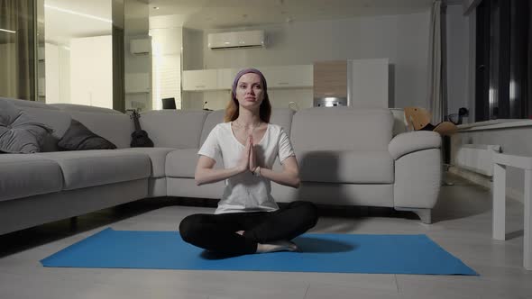 A Girl Sits in a Lotus Pose and Meditates on a Blue Yoga Mat in Her Apartment