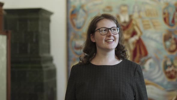 Pretty Woman with Glasses Smiles Looks at Camera and Around in Historical Hall alt