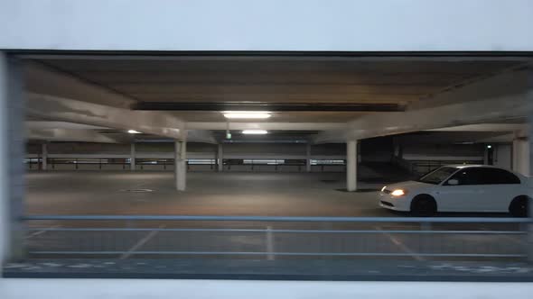 Drone shot of a car driving in a dark multi-story carpark alt
