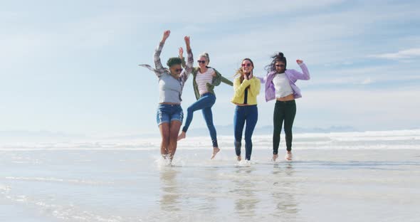 Happy group of diverse female friends having fun, dancing and smiling at the beach alt