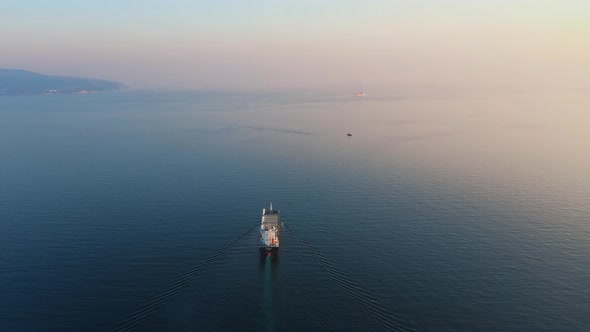 Aerial View Following the Ultra Large Cargo Ship at Sea Leaves Port at Sunset alt