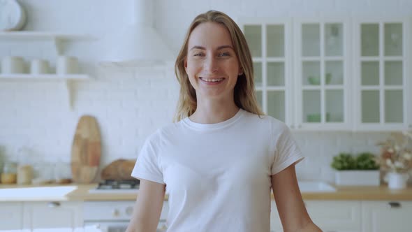 Happy Young Woman with Braces Smiles in the Background of Her Kitchen, Looking at the Camera alt