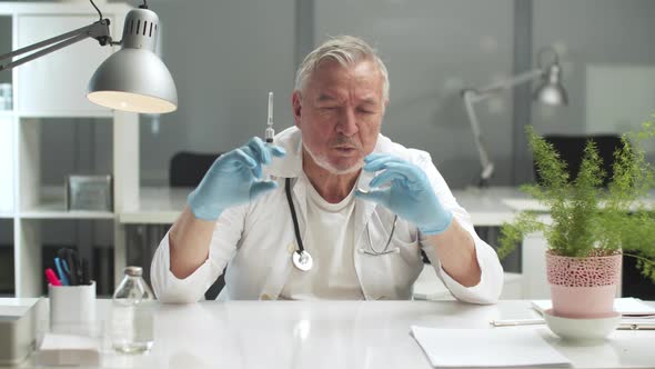 An Elderly Doctor with a Syringe and a Bottle in His Hands is Preparing to Administer Medication to