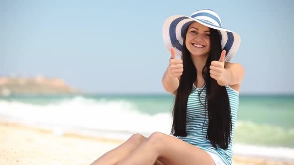 Smiling girl in hat show OK gesture on sand on beach in summer
