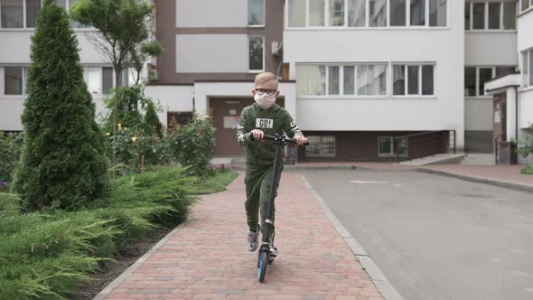 The boy rides a scooter during the quarantine period in a protective mask. alt