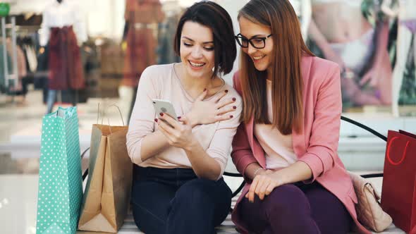 Joyful Young Women Are Using Smartphone Together Looking at Screen Smiling and Laughing Resting on alt