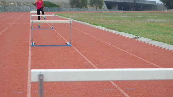 Caucasian female athlete running over hurdles on a running track at sports venue 4k alt