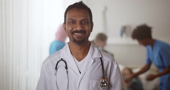 Portrait of Mature Indian Doctor Looking at Camera and Talking in Hospital Ward alt