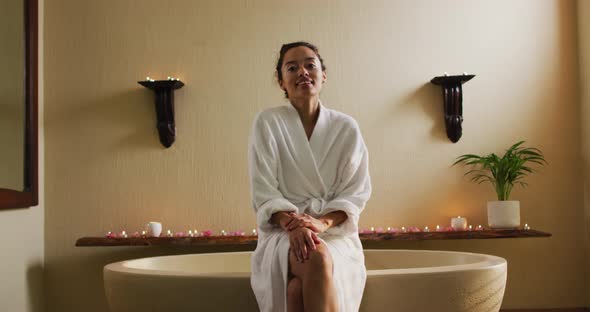 Happy biracial woman sitting in robe on bathtube alt