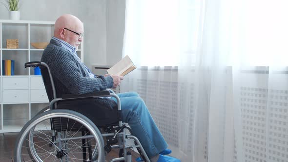 Disabled old man is sitting in a wheelchair at home alone. A handicapped person. alt