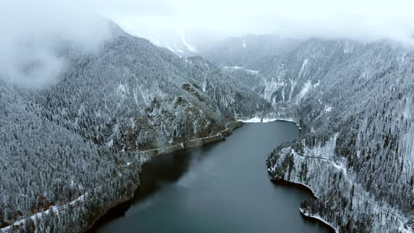 Lake in the mountains surrounded by forest in winter season. Flying above alt