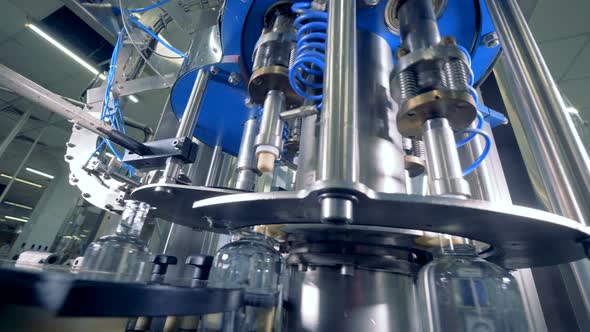 Moving Bottles Get Caps at a Plant, Close Up. Automated Industrial Equipment. alt