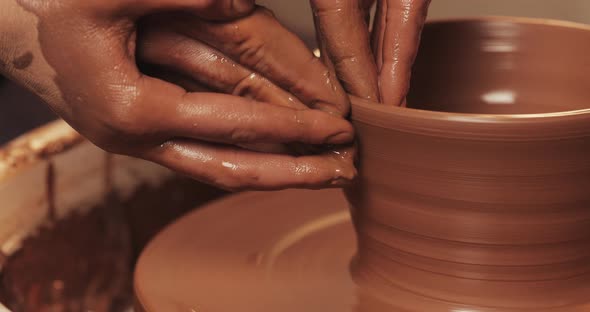 Hands of Couple Form a Pot of Clay on a Potter's Wheel. A Female Hand Helps a Man's Hands Shape alt