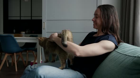 Female Cat Owner is Stroking and Caressing Her Cute Pet Sitting on Couch in Living Room alt