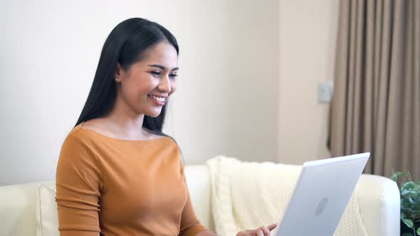 Young woman sitting on sofa using laptop for work at home