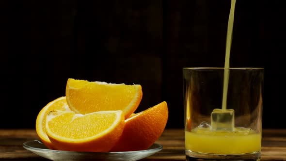 Juice Is Poured Into A Glass With Ice, Several Sliced Oranges In A Plate