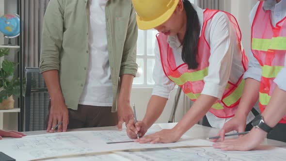 Three Asian Engineers With Helmets Helping A Man Drawing Building Construction At The Office alt