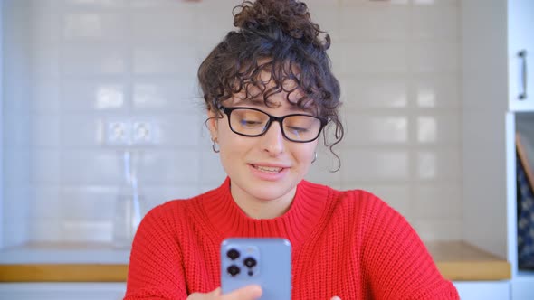 Curly brunette speaking on frontal camera of smart phone in 4k video alt